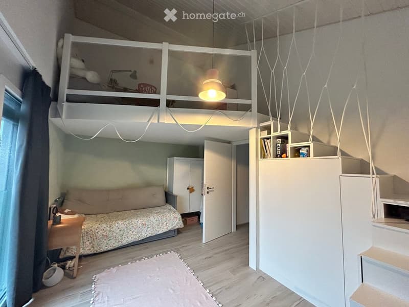 Cozy bedroom with a single bed, nightstand, lamp, bookshelf, and a lofted bunk bed above. Features wooden flooring, white walls, and modern lighting.