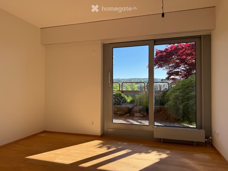 Unfurnished Room. Empty room with wooden flooring, large sliding glass doors leading to a garden area, and natural light streaming in.