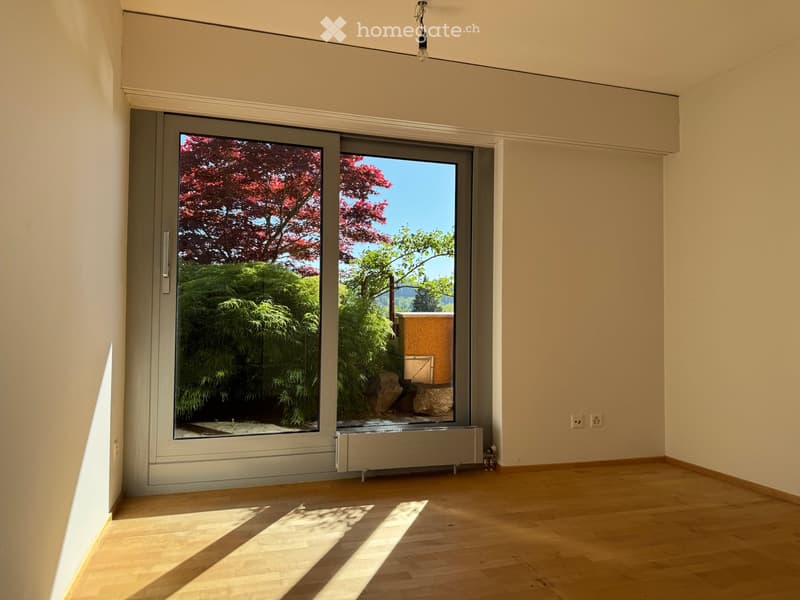 Unfurnished Room. Empty room with wooden flooring, large sliding glass doors leading to a garden, and natural light streaming in.