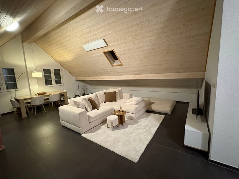 Modern living room with a sectional sofa, coffee table, small stool, dining area with table and chairs, and large windows.