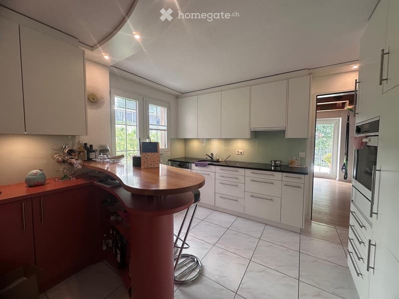 Modern kitchen with white cabinets, a central island with a wooden countertop, and a red base. Features include a sink, oven, and various decorative items on the counter.