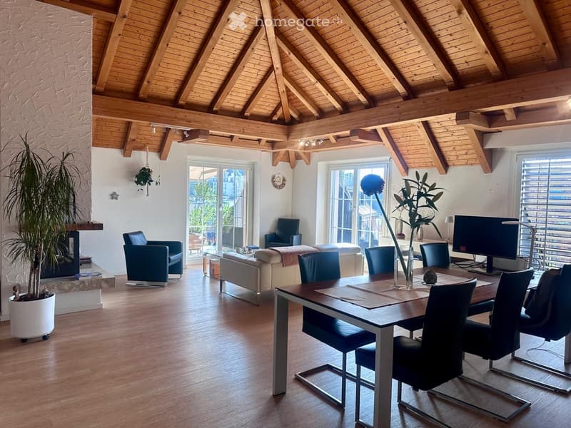 Open-plan living and dining area with exposed wooden beams, a fireplace, a sofa, chairs, a dining table, and a TV screen.