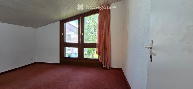 Empty room with wooden flooring, white walls, large window with curtains, and a door.