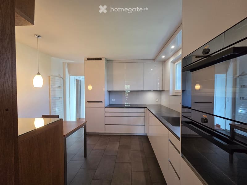Modern kitchen with white cabinets, dark countertops, and a wooden dining table.