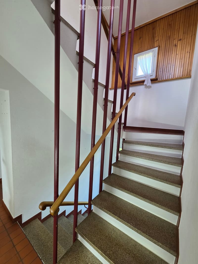 Staircase with wooden handrail and metal balusters, leading to an upper level with a window and wooden paneling.