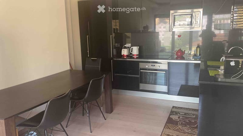 Modern kitchen with dark cabinets, stainless steel appliances, a wooden dining table with four chairs, and a small rug on the floor.