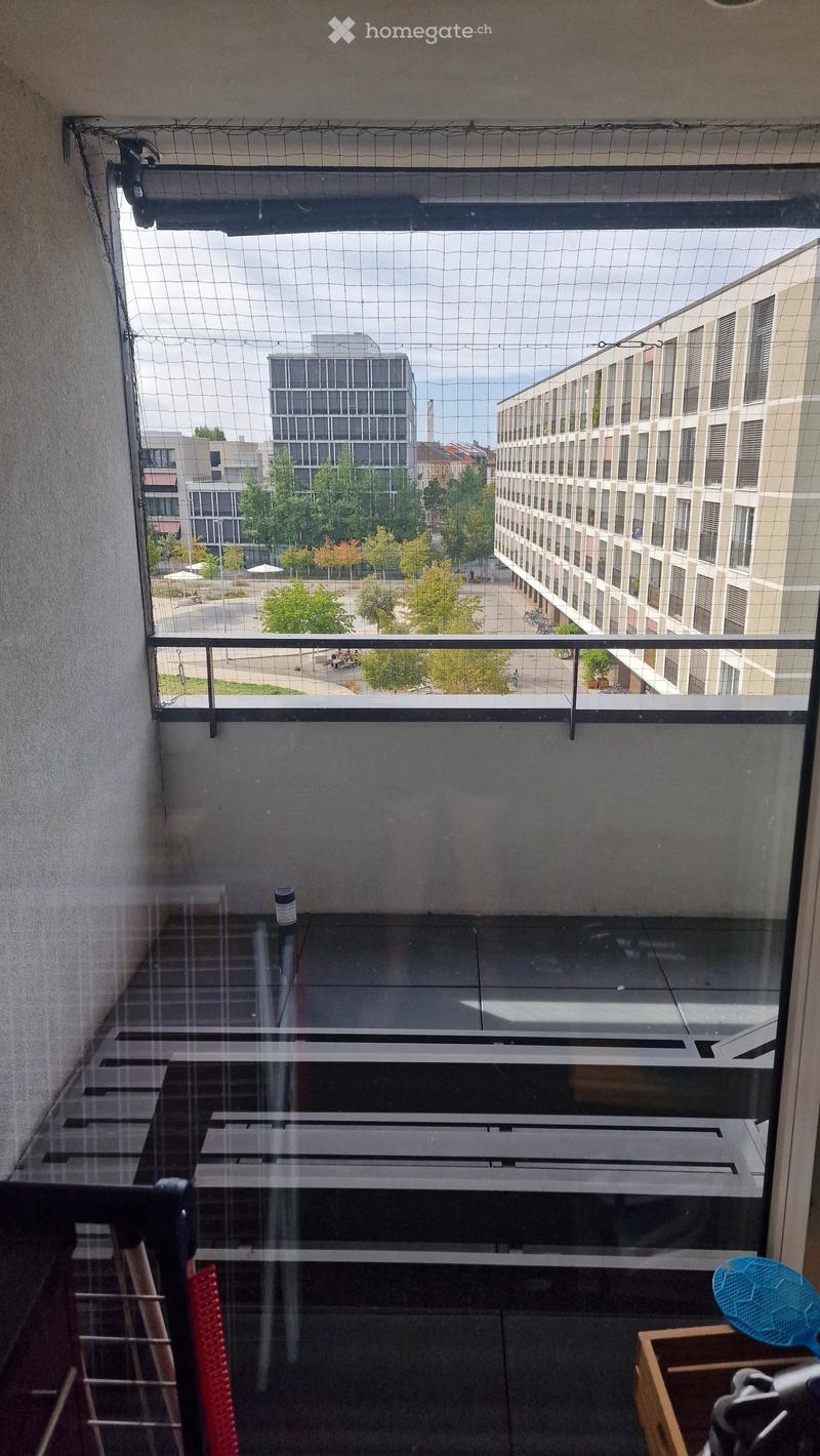 Balcony with a metal railing and a net cover, overlooking a cityscape with modern buildings and greenery.