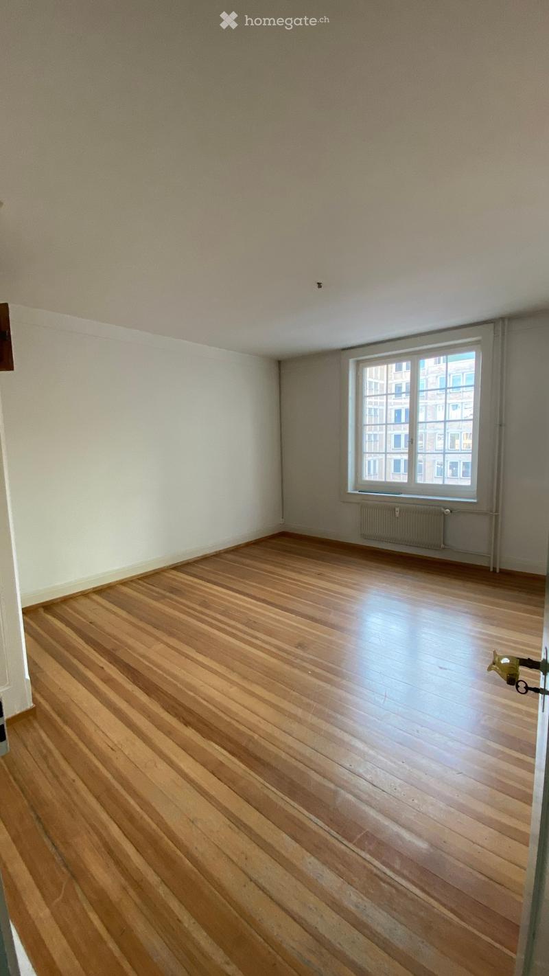 Empty room with wooden flooring, white walls, and a large window with a radiator below it.