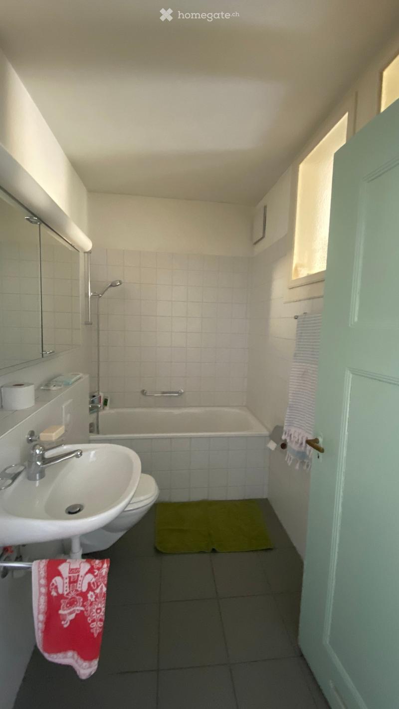 Bathroom with a sink, toilet, bathtub, and a small window. Includes a towel and a bathmat on the floor.