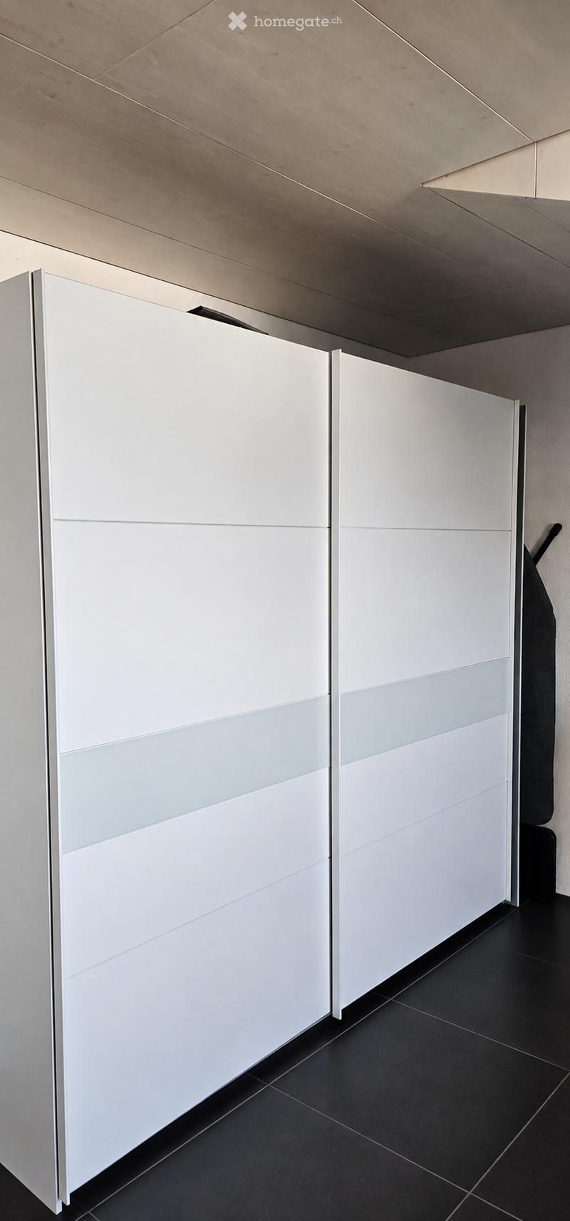 Modern, minimalist room with white sliding closet doors and black tiled flooring. The space is completely empty, with no furniture or personal items visible.
