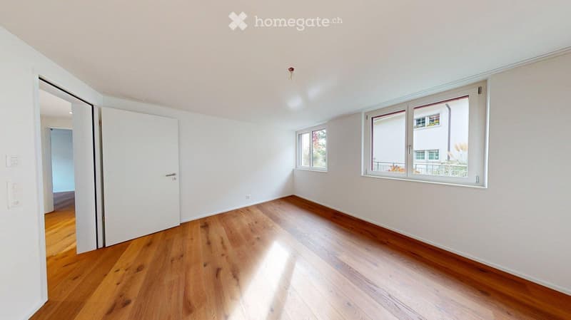 Empty room with wooden flooring, white walls, and large windows allowing natural light. No furniture or furnishings are present.