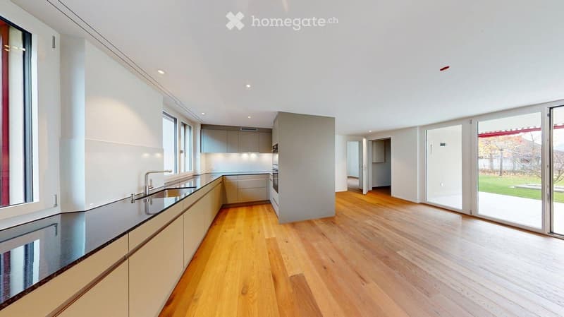 Modern kitchen with light-colored cabinets, a stainless steel sink, and wooden flooring. Large windows and sliding glass doors lead to an outdoor area.