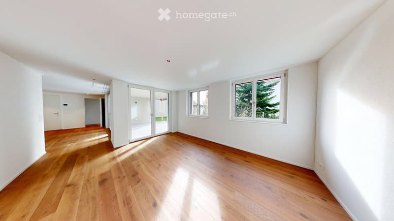 Empty room with wooden flooring, white walls, large windows, and sliding glass doors leading to an outdoor area.