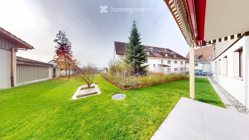 Well-maintained garden with green lawn, small tree, and surrounding residential buildings.