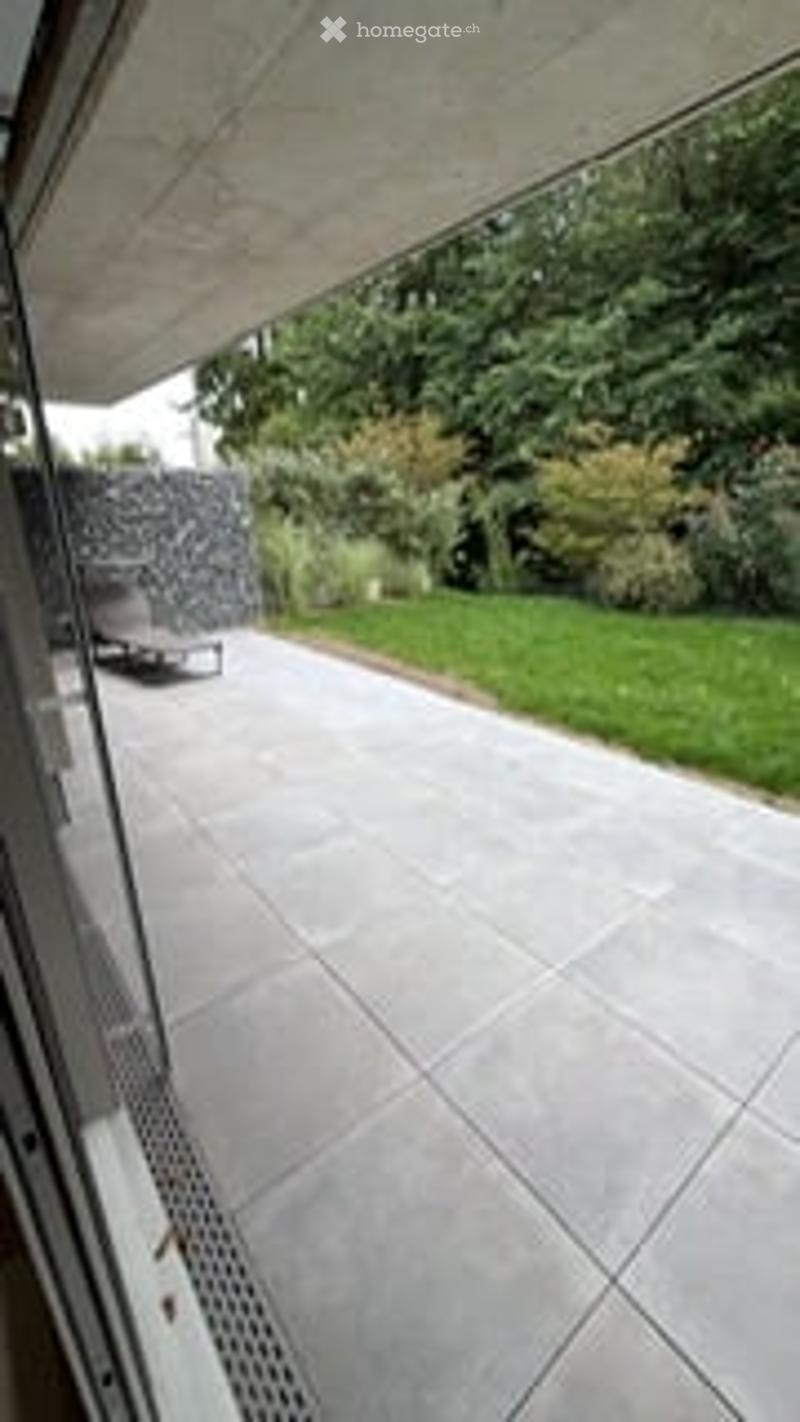 Modern patio with large concrete tiles, lounge chair, and lush greenery in the background.