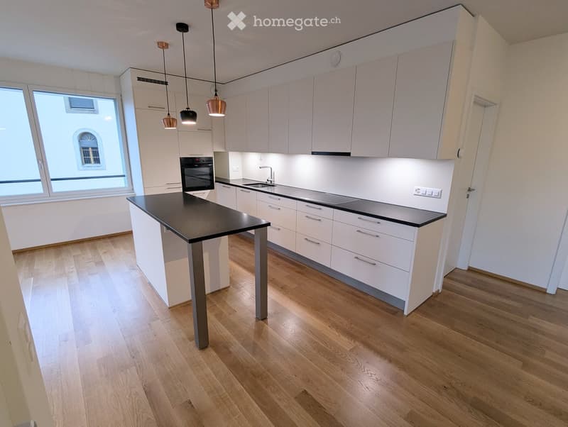 Modern kitchen with white cabinets, black island, wooden flooring, and pendant lights.