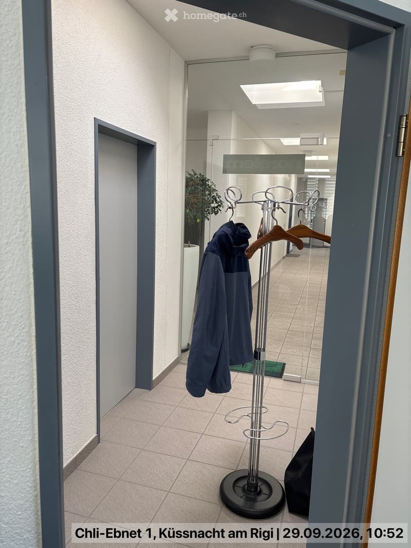 Modern hallway with tiled floor, white walls, coat rack with jackets, and a small green mat near the entrance.