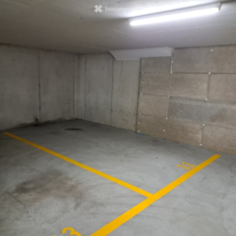 Empty underground parking space with concrete walls and floor, marked parking spaces with yellow lines.