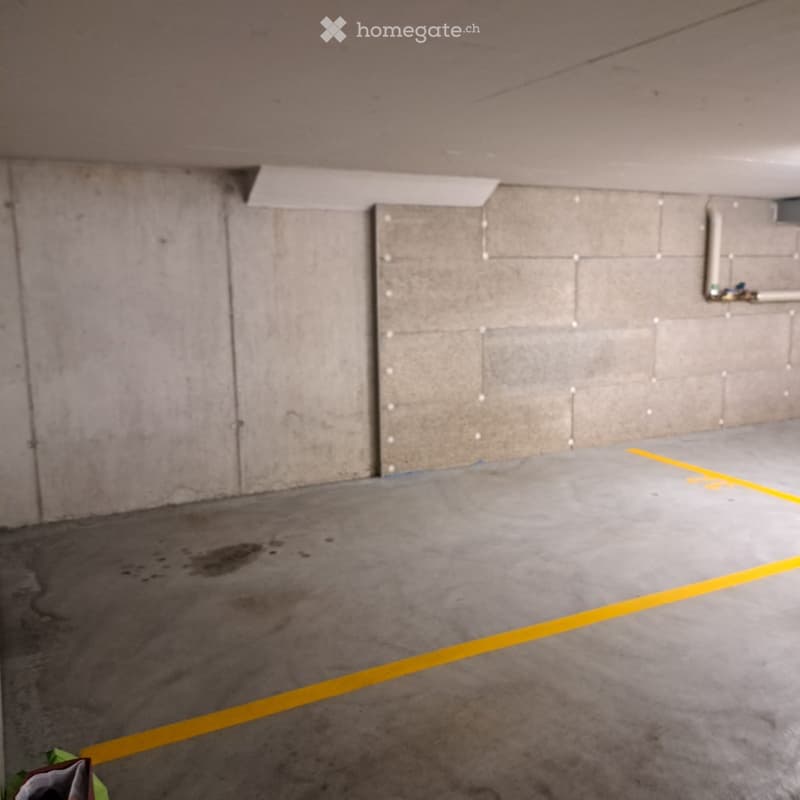 Empty underground parking space with concrete walls, floor, and yellow parking lines.