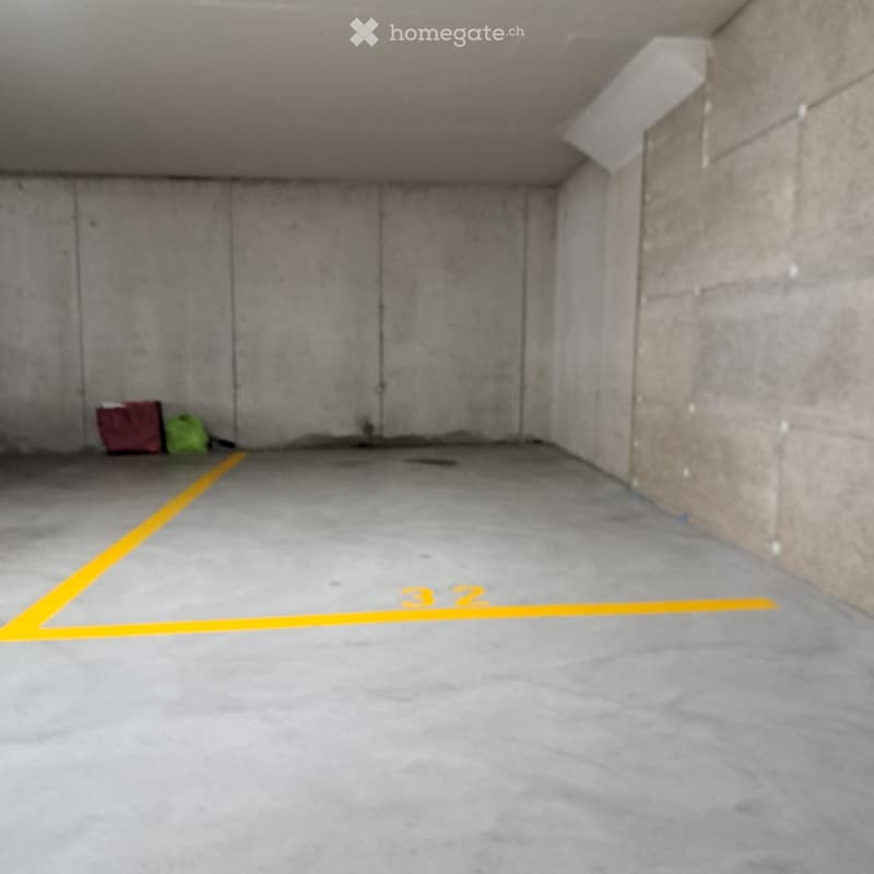 Empty underground parking space with concrete walls and floor, marked parking spot number 32, and two bags placed against the wall.