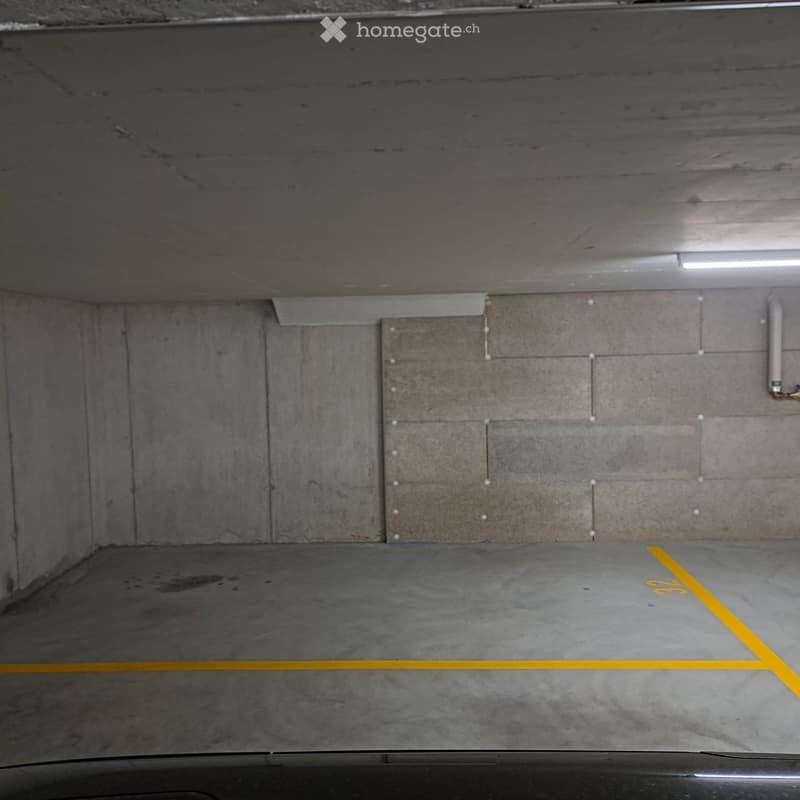 Empty underground parking space with concrete walls and floor, marked parking spots, and overhead lighting.