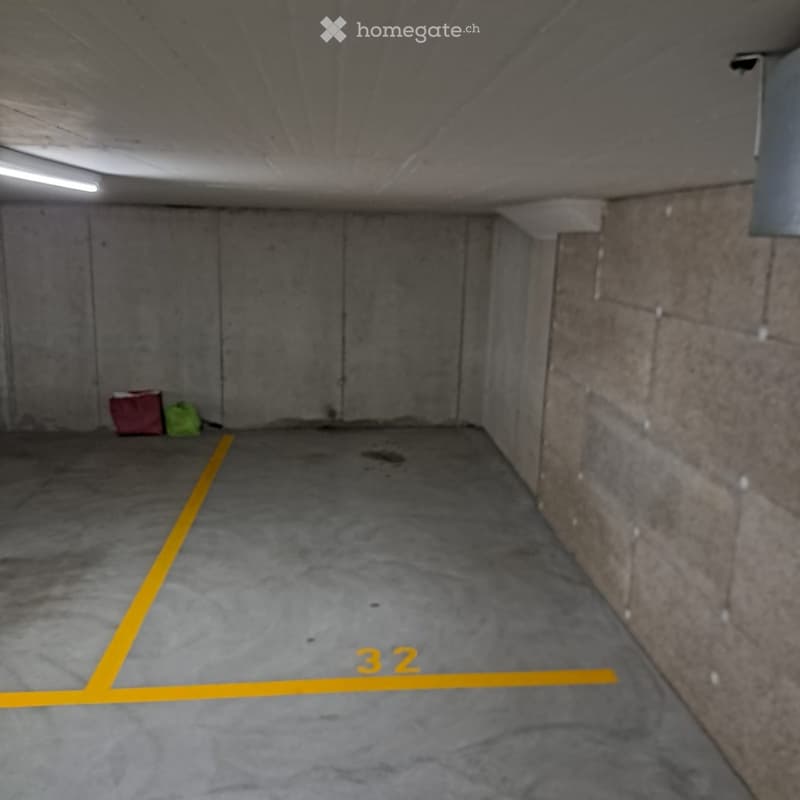 Underground parking space with concrete walls and floor, marked parking space number 32, small items in corner.