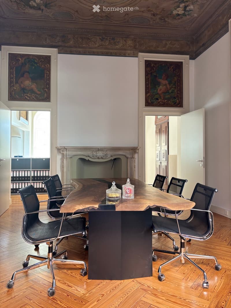 Elegant room with a large wooden table, black office chairs, fireplace, and paintings on the walls.