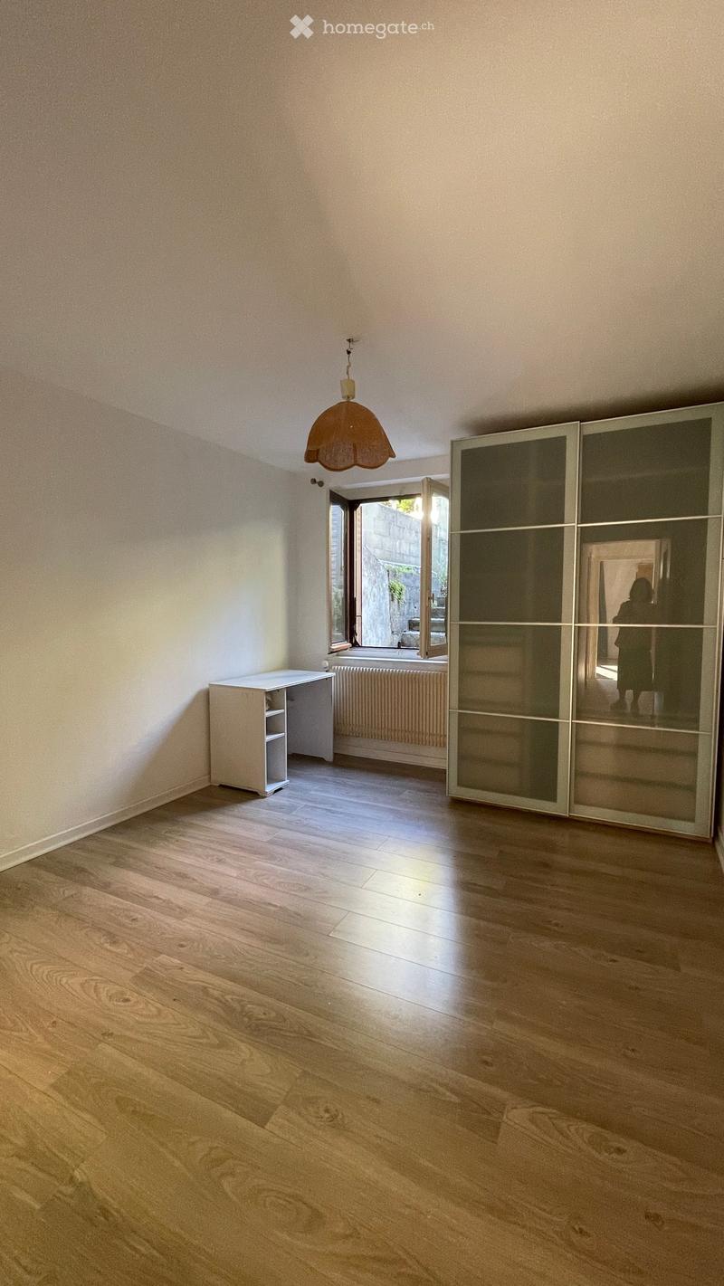 Empty room with wooden flooring, white walls, a hanging lamp, a sliding wardrobe, a small desk, and a window with a radiator below it.