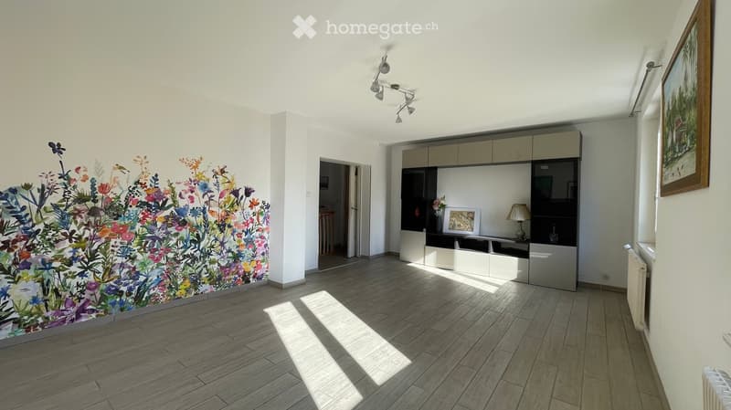 Bright room with wooden flooring, white walls, and a large floral mural. Features a modern cabinet with glass doors, a small table lamp, and a framed picture on the wall.