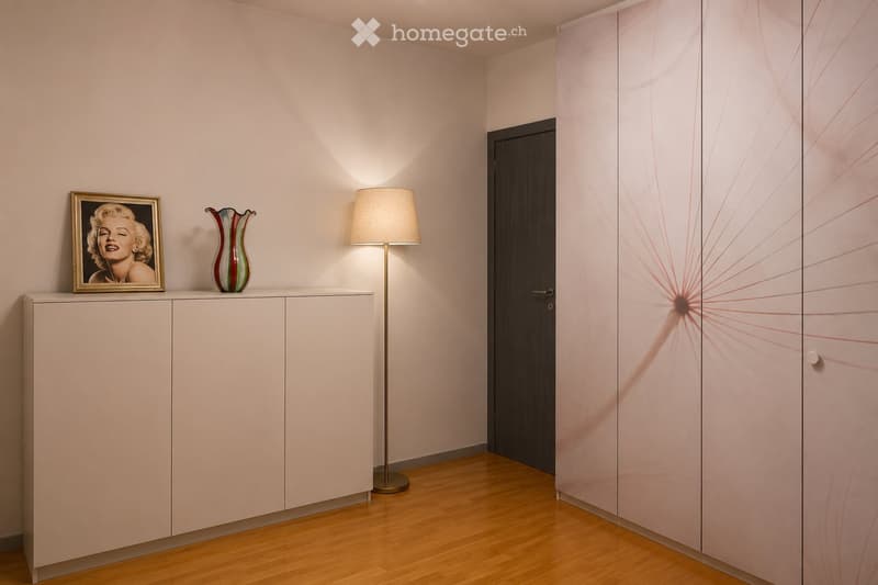 A modern, minimalist room with light-colored walls, a wooden floor, a white cabinet, a floor lamp, a picture frame, and a decorative vase.