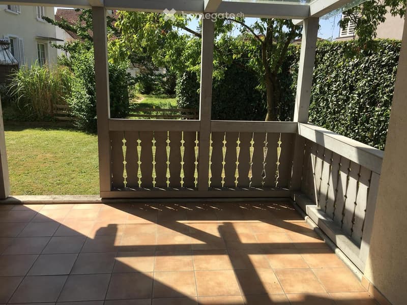 Balcony with railings, tiled floor, green lawn and trees in the background