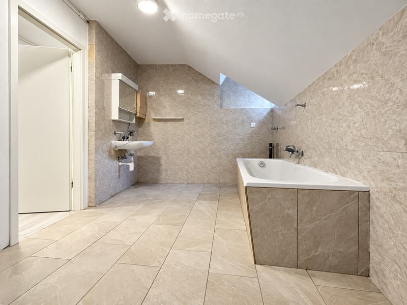 Modern bathroom with beige marble tiles, a freestanding bathtub, a wall-mounted sink, and a mirrored cabinet.