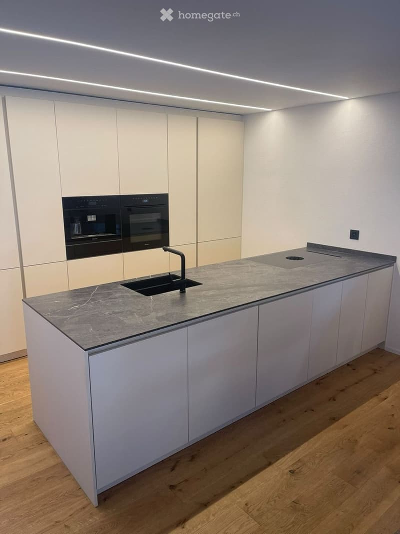 Modern kitchen with white cabinets, a marble countertop, a sink with a faucet, and built-in ovens.