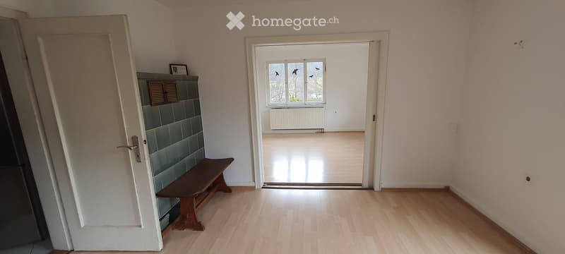 Empty hallway with wooden flooring, white walls, a bench, and a door leading to another room.