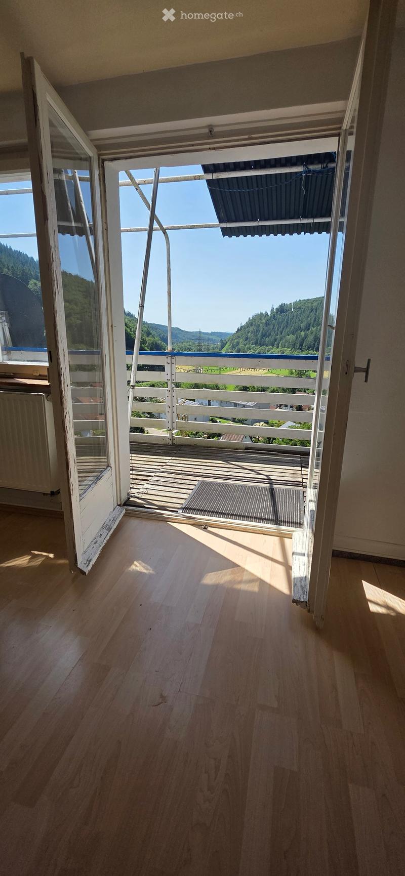 Open wooden balcony with white railings, overlooking a scenic valley with trees and hills.
