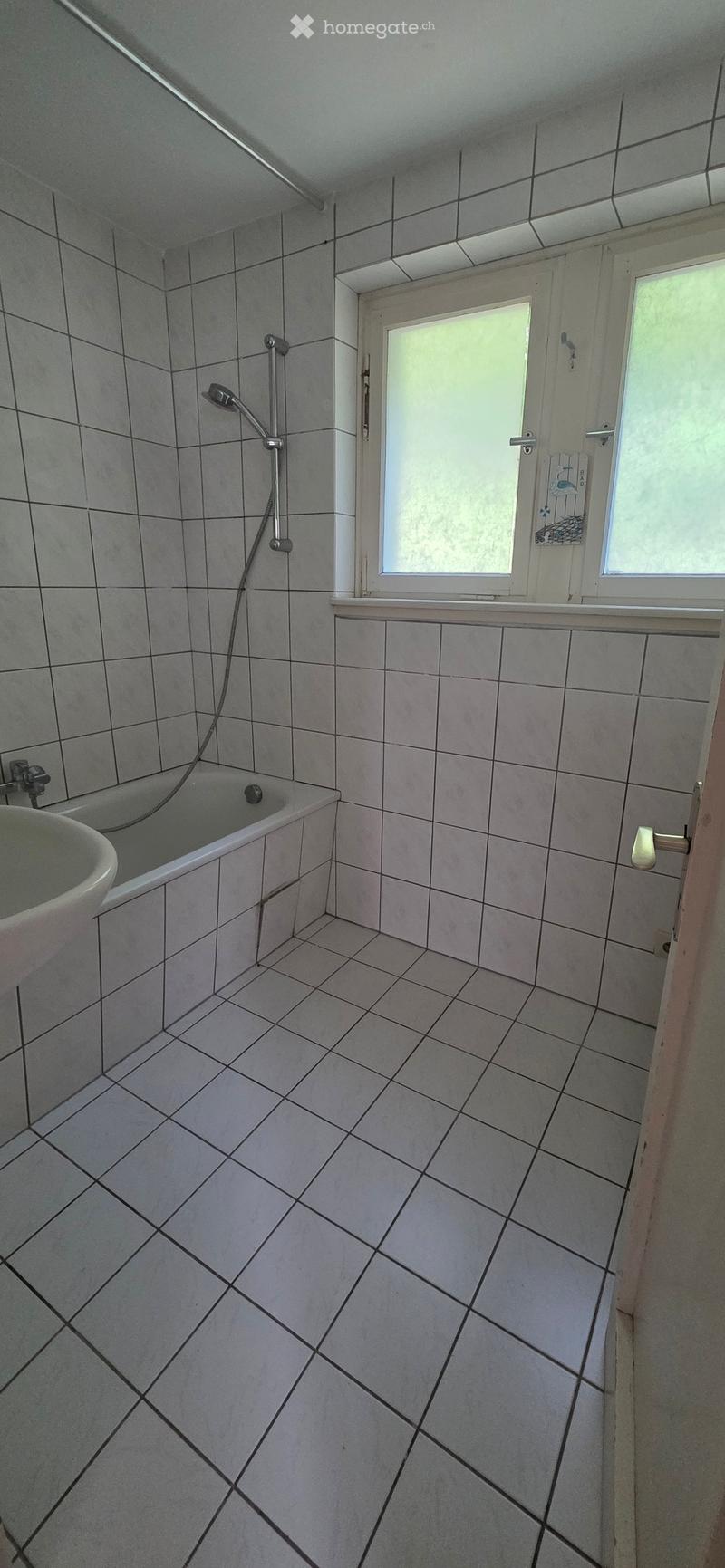 Bathroom with tiled walls and floor, featuring a bathtub, sink, and shower fixture.