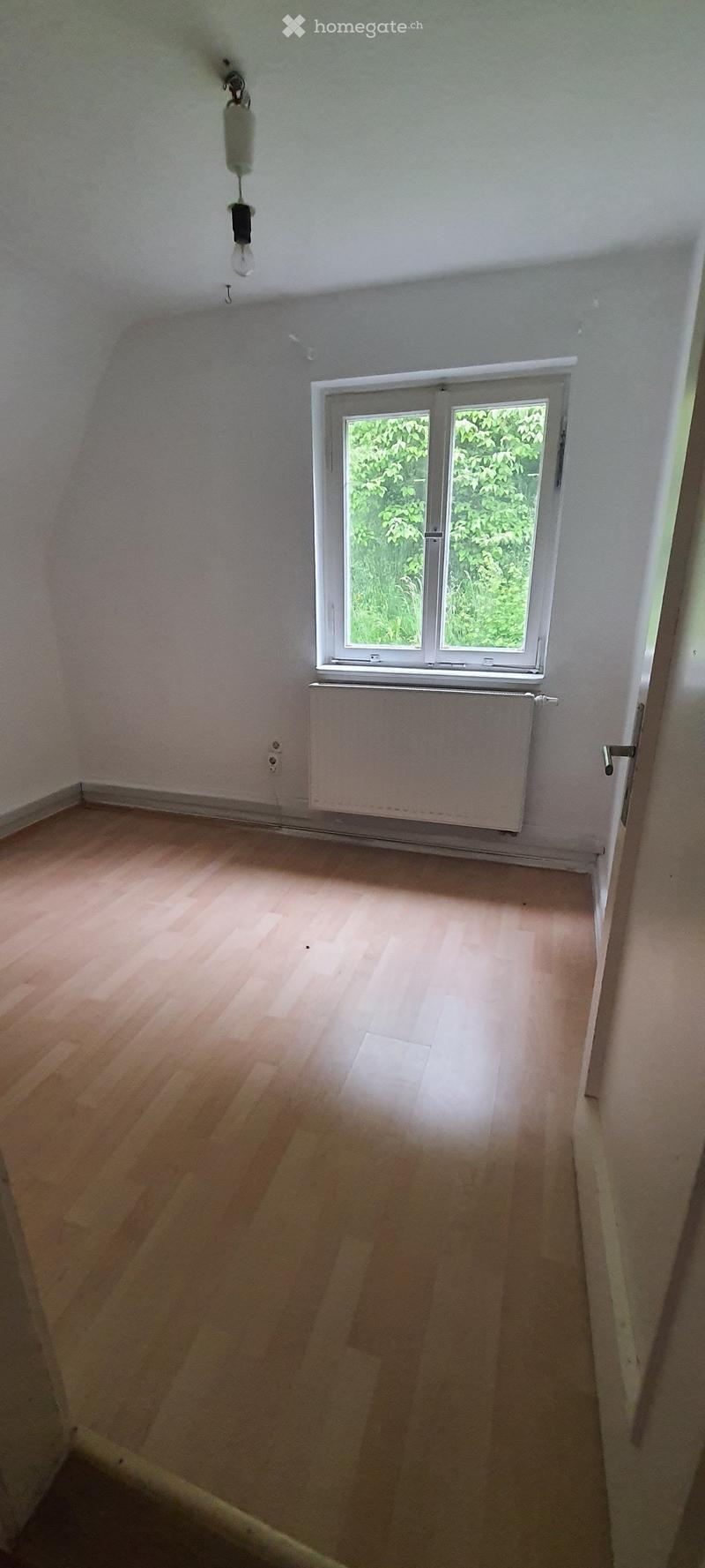 Empty room with wooden flooring, white walls, a single window with white frame, and a radiator below the window. No furniture or equipment present.