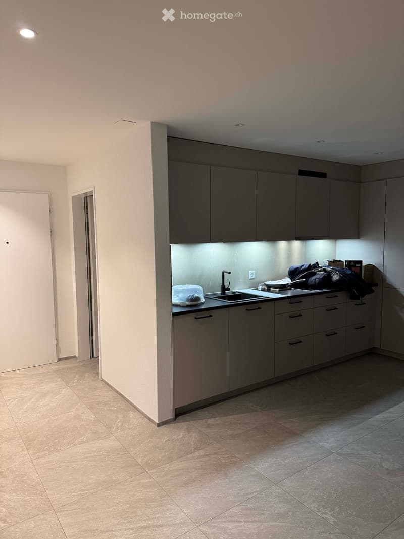 Modern kitchen with grey cabinets, a sink, and a countertop. The space is clean and organized with tiled flooring and recessed lighting.