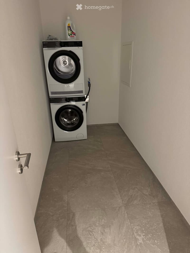 Empty room with tiled floor and white walls, featuring a stacked washer and dryer unit in the corner.