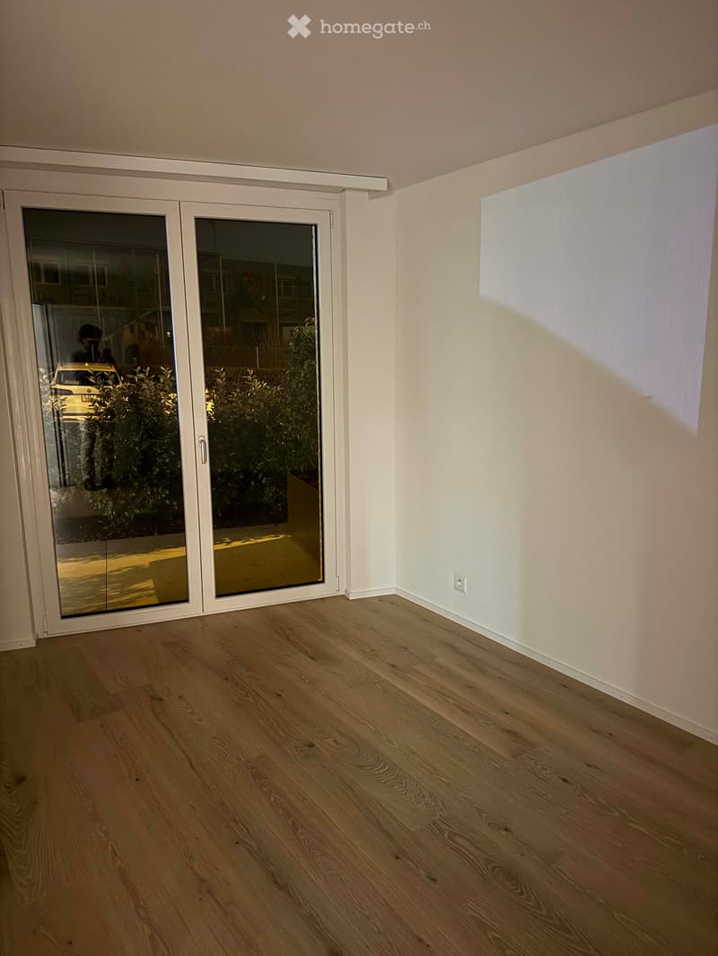Empty room with light wooden flooring and white walls, featuring a large sliding glass door leading outside.