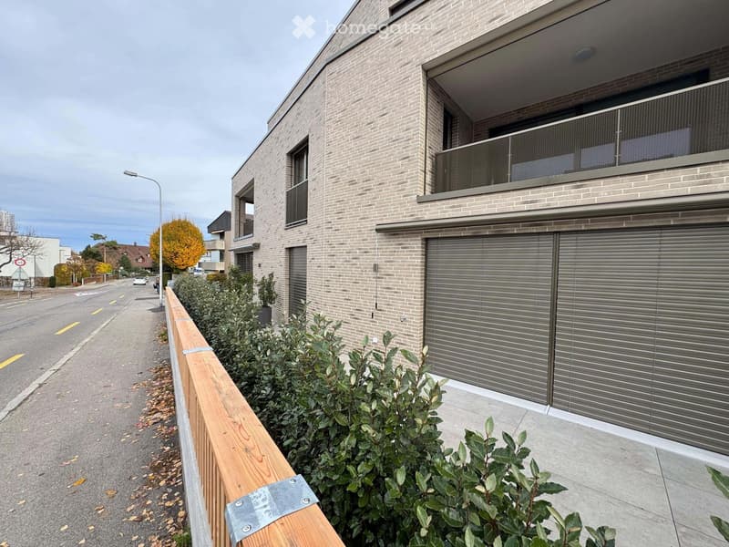Modern two-story brick building with large windows, a balcony, and a garage entrance with roller shutters.