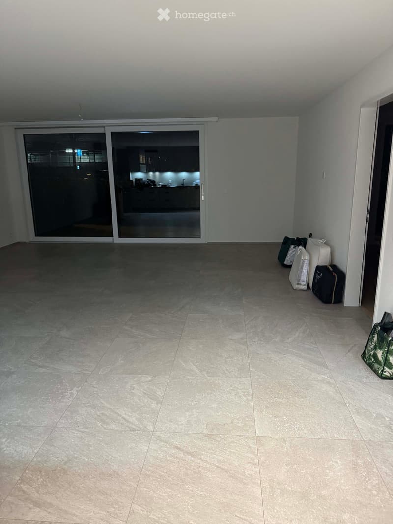 Empty room with tiled floor, large sliding glass doors leading to another room, and a few bags placed near the wall.