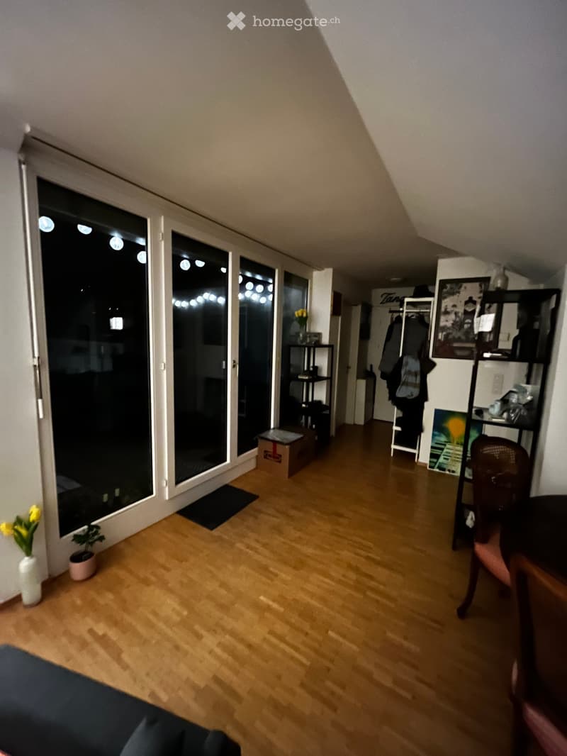 A furnished room with wooden flooring, large windows, a chair, shelves, and decorative vases.