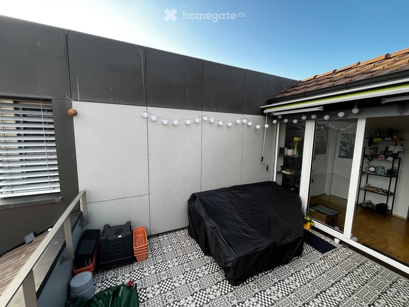 Balcony with patterned tile flooring, covered grill, and string lights, connected to an indoor space with shelves and decor.