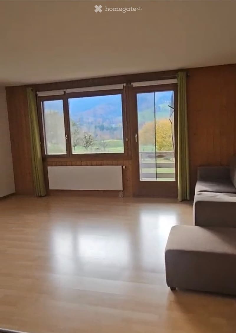 Spacious room with wooden flooring, large windows offering a scenic view, and a single sofa in the corner.