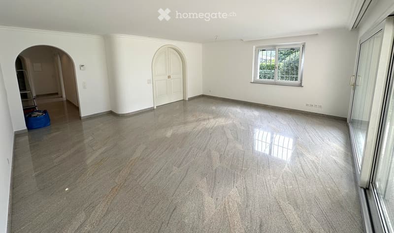 Empty room with polished marble floors, white walls, large window, and arched doorway leading to another space.