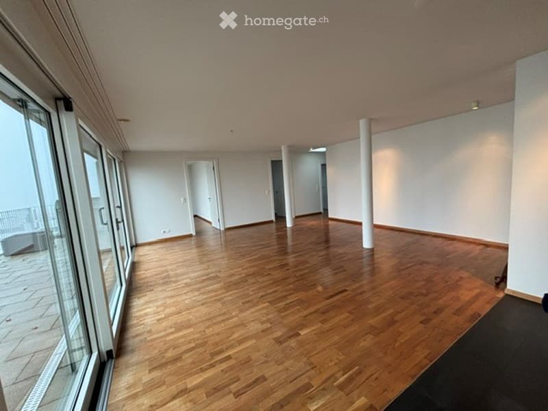 Empty room with wooden flooring, large windows offering a view, and white walls.