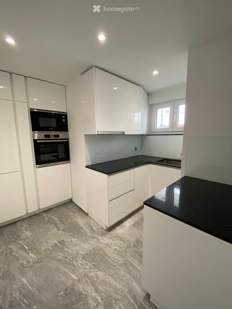 modern kitchen, white cabinets, black countertops, built-in oven, microwave, dishwasher, stainless steel appliances, marble flooring