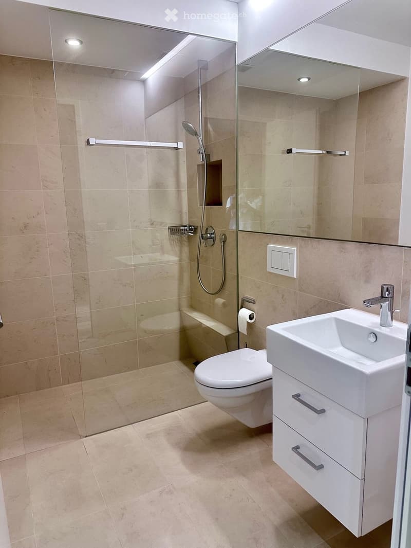 Modern bathroom with beige tiles, a glass-enclosed shower, a toilet, a sink with a modern faucet, and a mirrored cabinet.