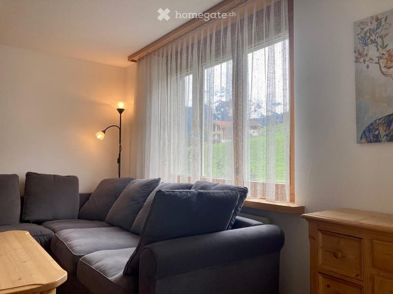 A living room with a couch, a lamp, a wooden table, and a window with curtains.